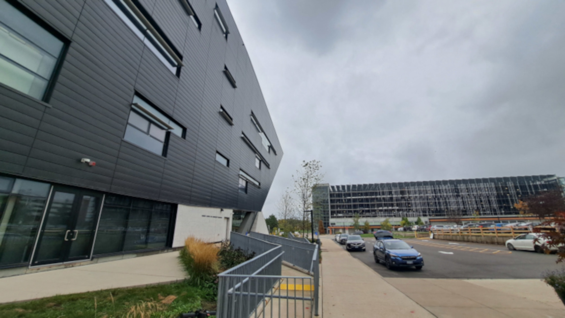 Two buildings with a parking lot, cars parked underneath a grey and cloudy sky. 