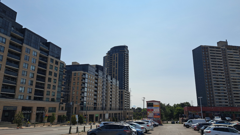Street view of Emery neighbourhood with high-rise buildings on both sides, parked cars and a sunny day.